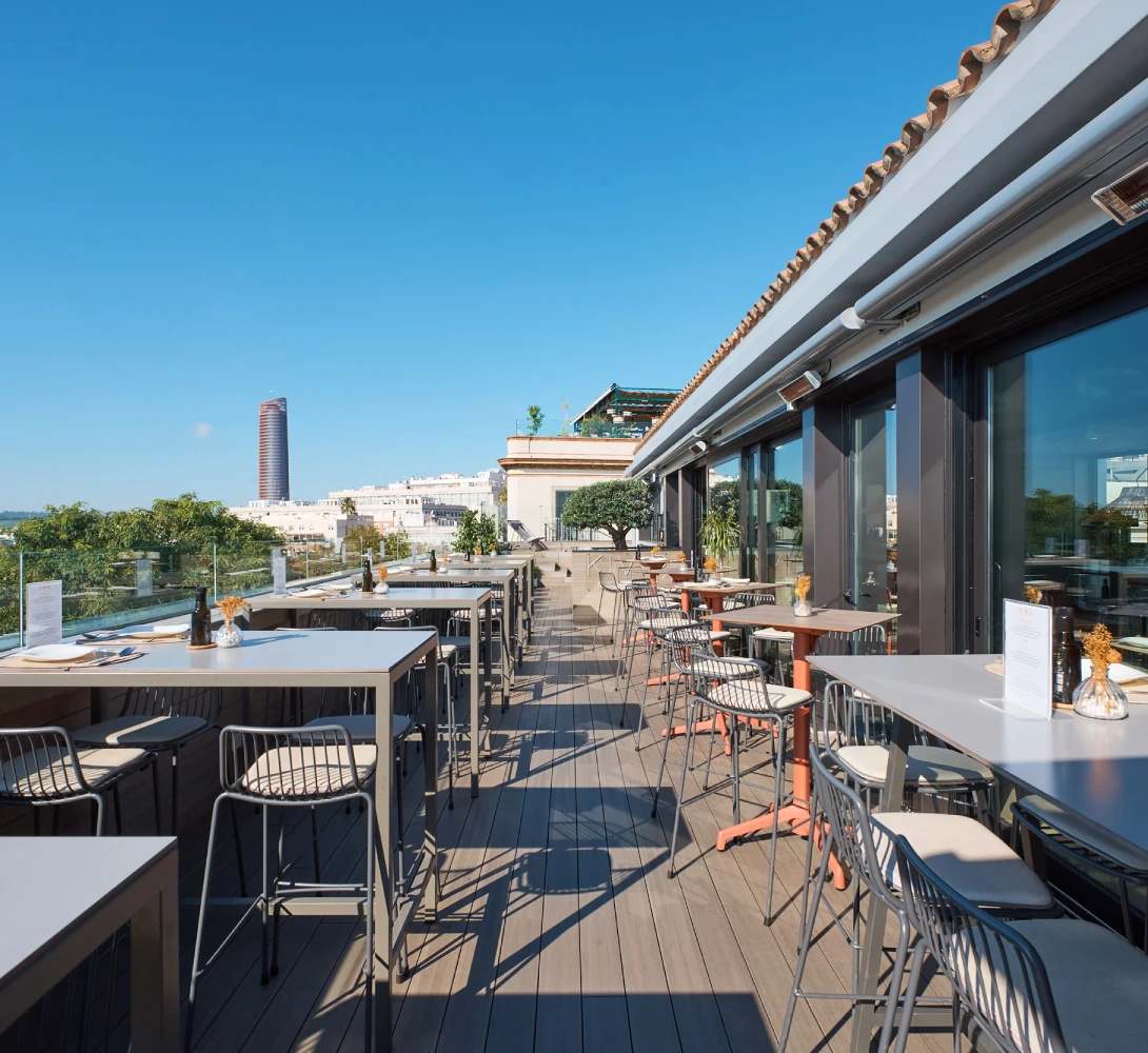 Terraza moderna con mesas y sillas, vista a la ciudad y cielo despejado.
