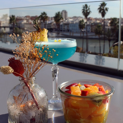 C&oacute;ctel azul y fruta en una terraza con vista a la ciudad.