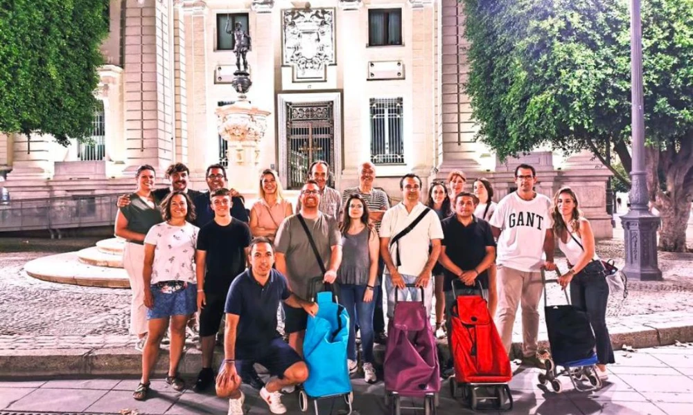 Grupo de personas posando con carritos frente a un edificio iluminado.