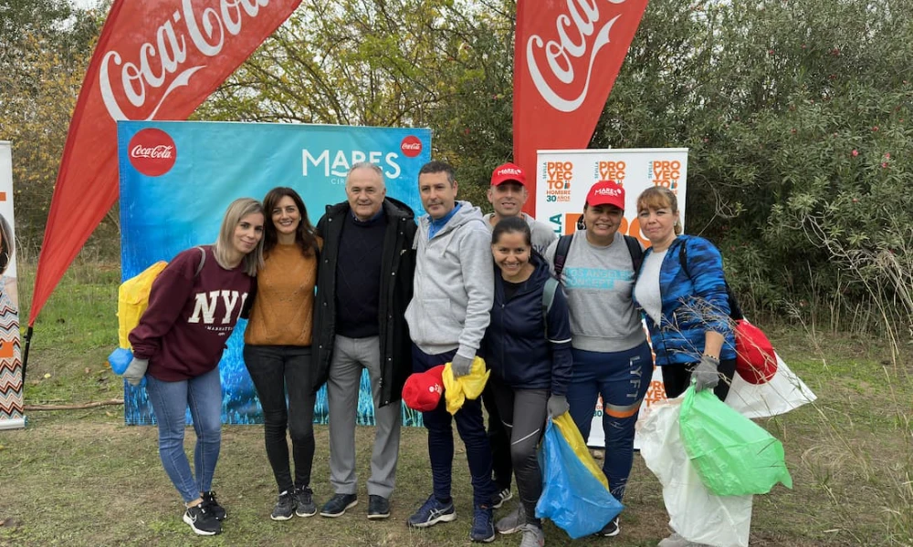 Grupo de personas posa frente a pancartas de Coca-Cola al aire libre.