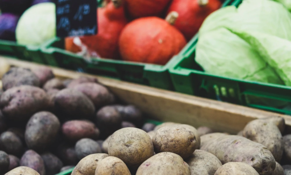 Verduras variadas en un mercado, incluyendo papas, col y calabazas.