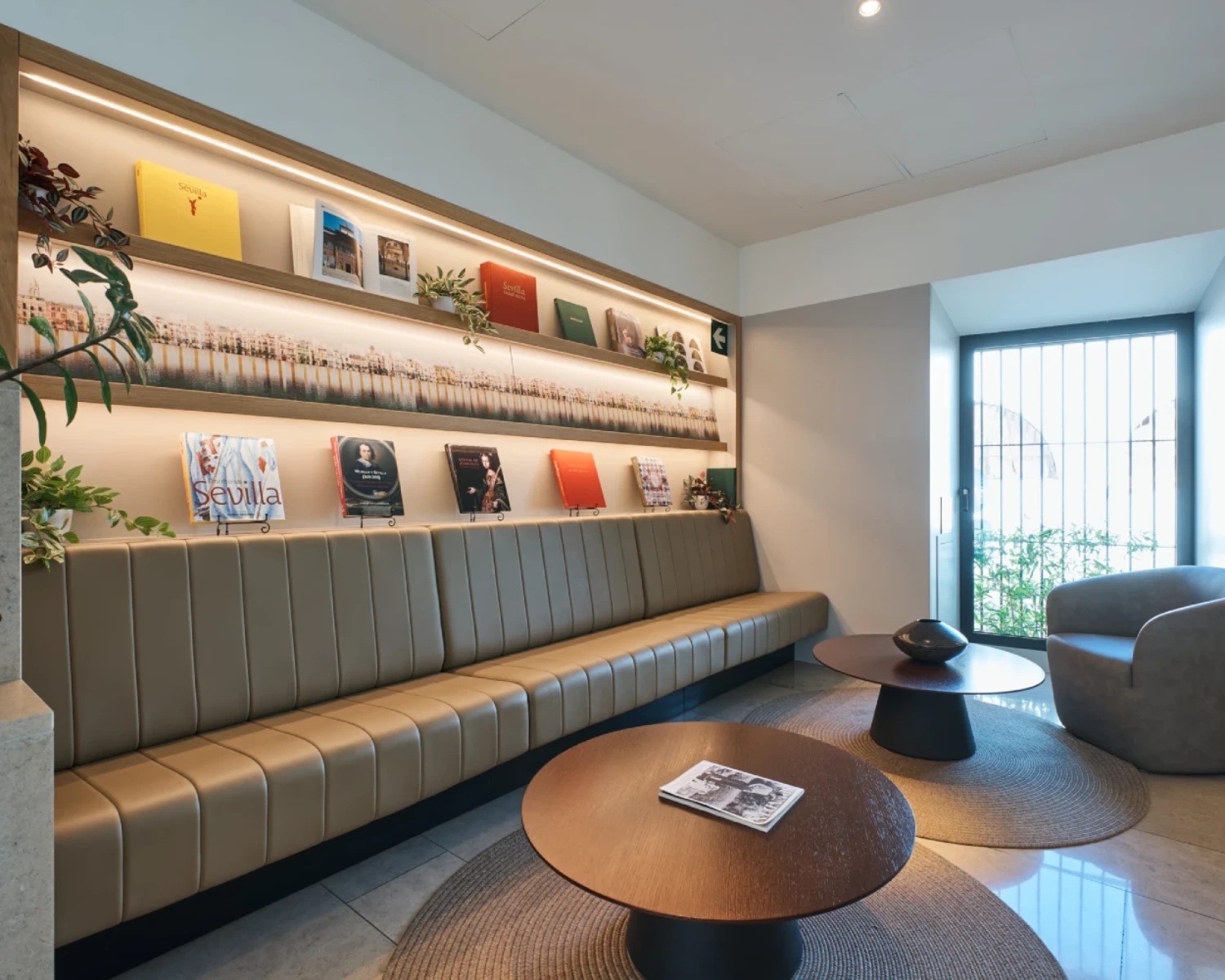 Sala de espera moderna con sof&aacute;, libros y mesas redondas.