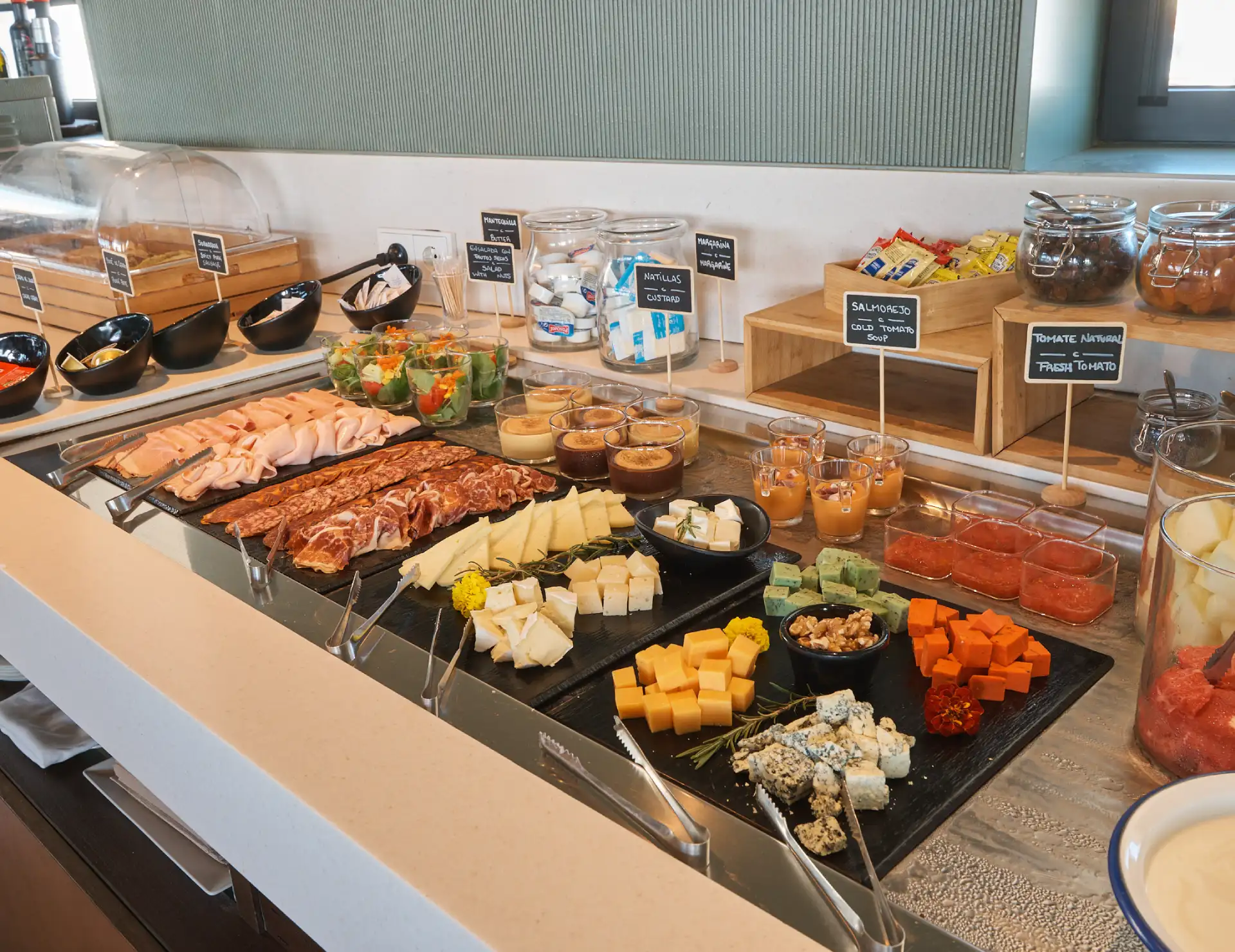Buffet con embutidos, quesos, ensaladas, natillas y salmorejo.