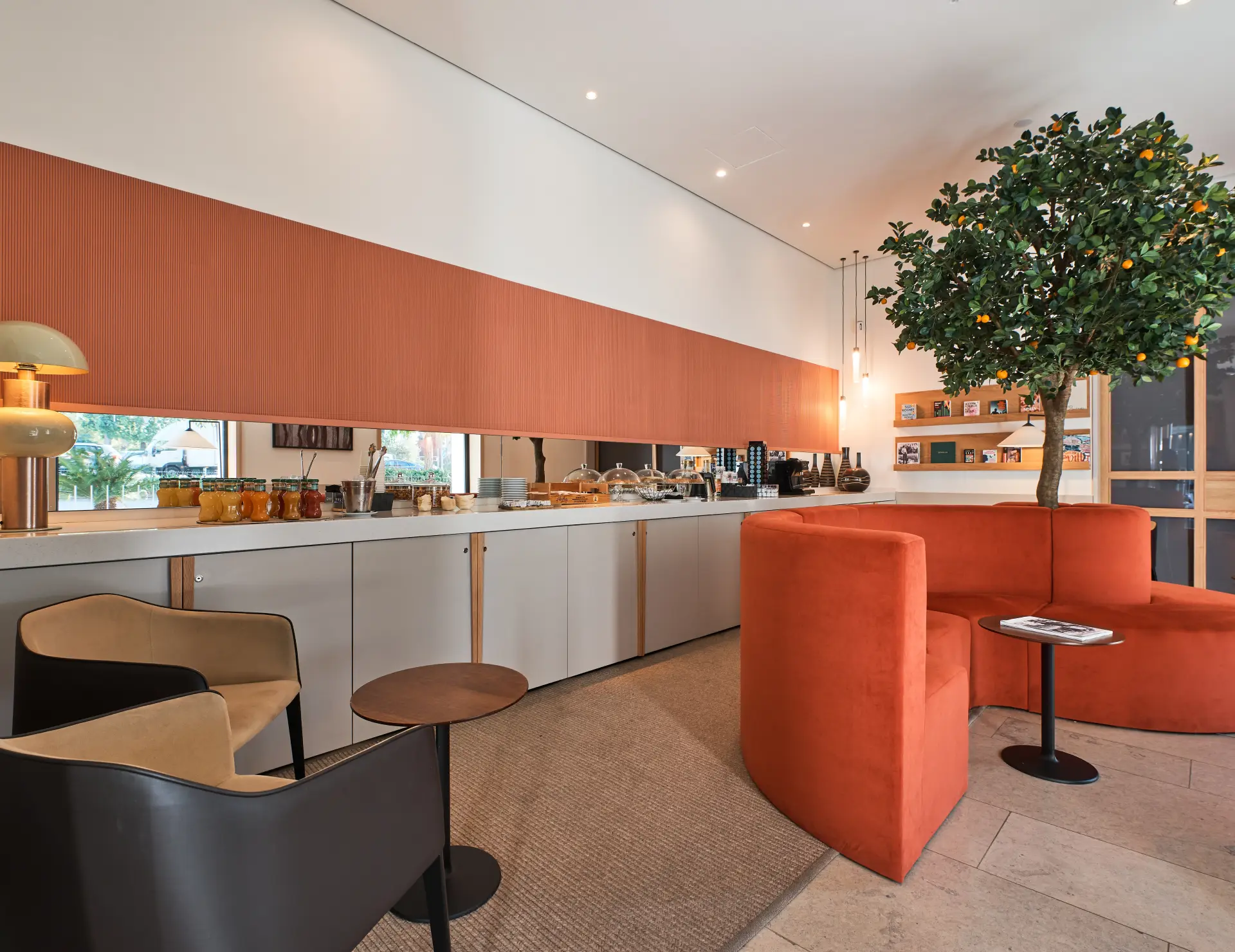 Sala moderna con sillas y sof&aacute; anaranjados, buffet al fondo y &aacute;rbol decorativo.