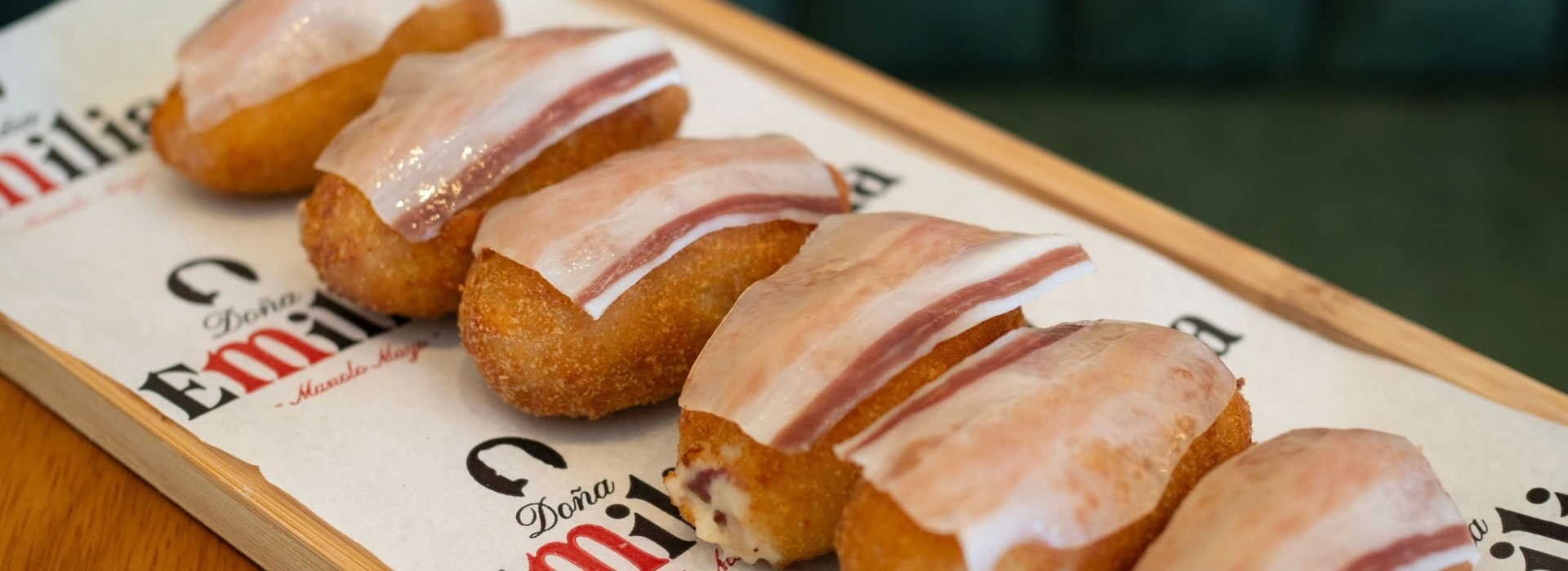 Croquetas empanizadas con l&aacute;minas de jam&oacute;n curado sobre papel decorado.