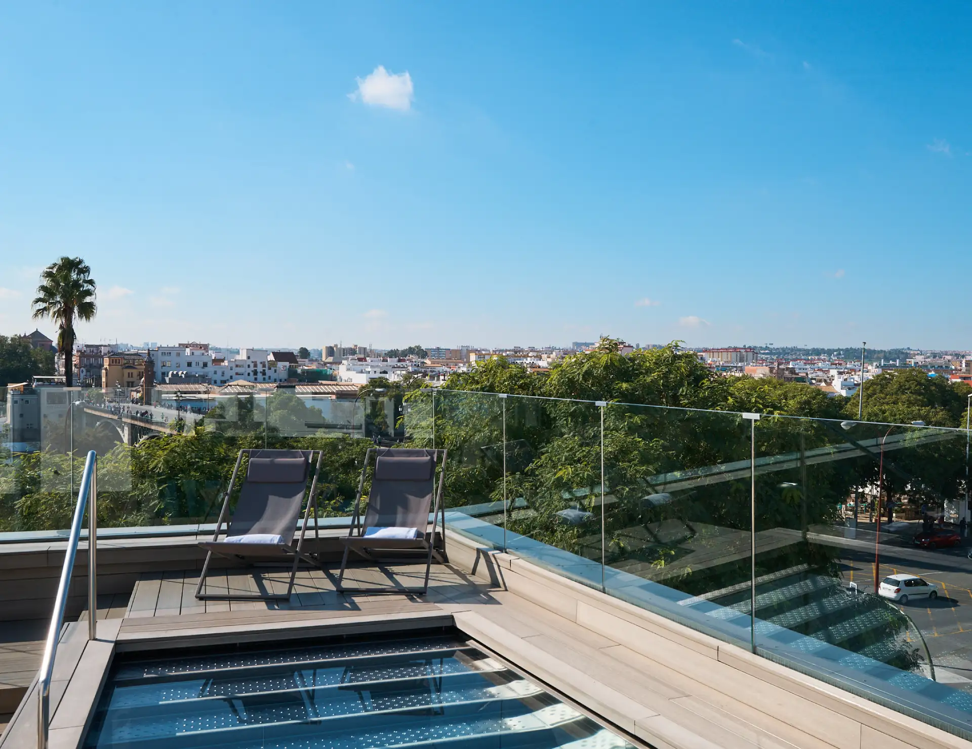 Terraza con vistas a la ciudad, dos sillas reclinables y cielo azul despejado.
