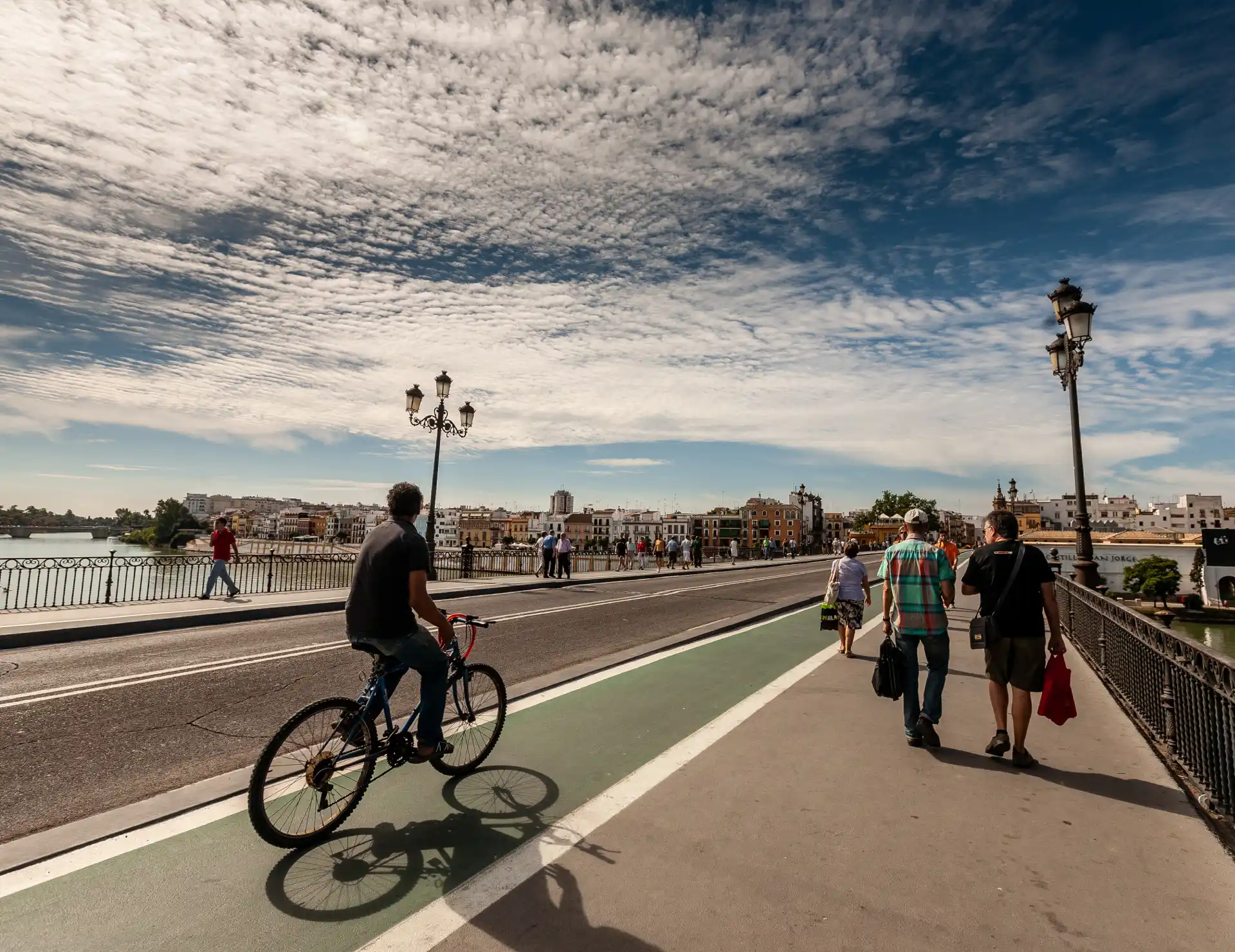 Persona en bicicleta y peatones cruzando un puente bajo un cielo nublado.