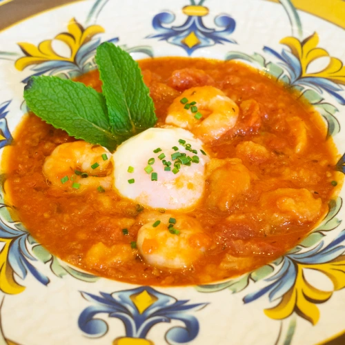 Guiso de camarones con huevo poch&eacute; y menta en un plato decorado.