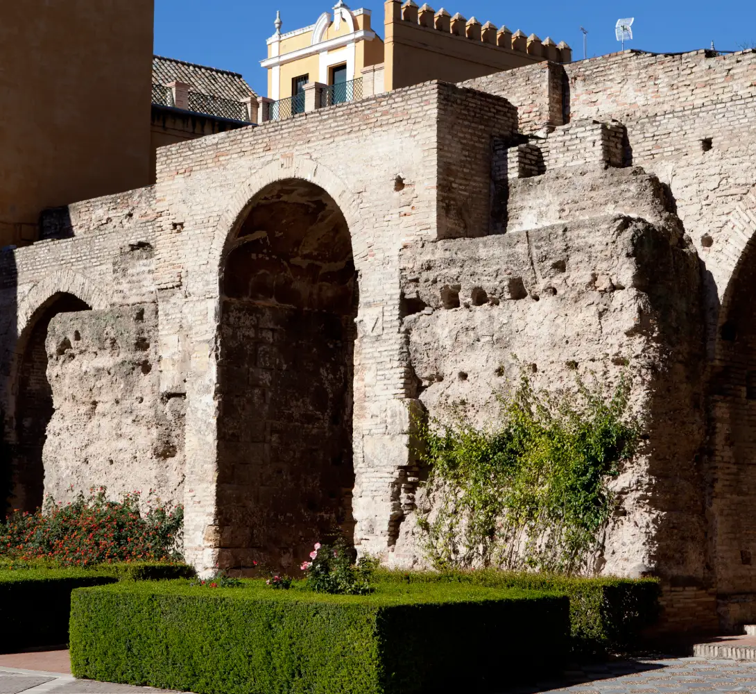Ruinas de un antiguo edificio de piedra con arcos, rodeado de vegetaci&oacute;n y arbustos.