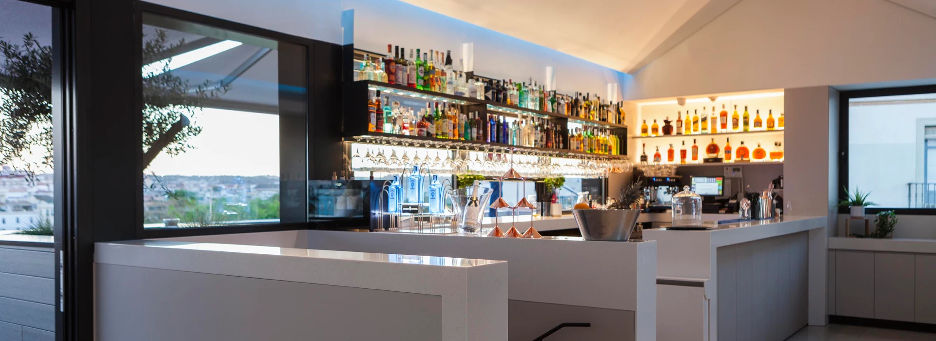 Bar moderno con botellas iluminadas en estanter&iacute;as y copas colgando arriba.