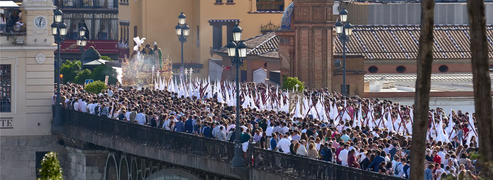 Multitud en procesi&oacute;n con nazarenos y trono en un puente.