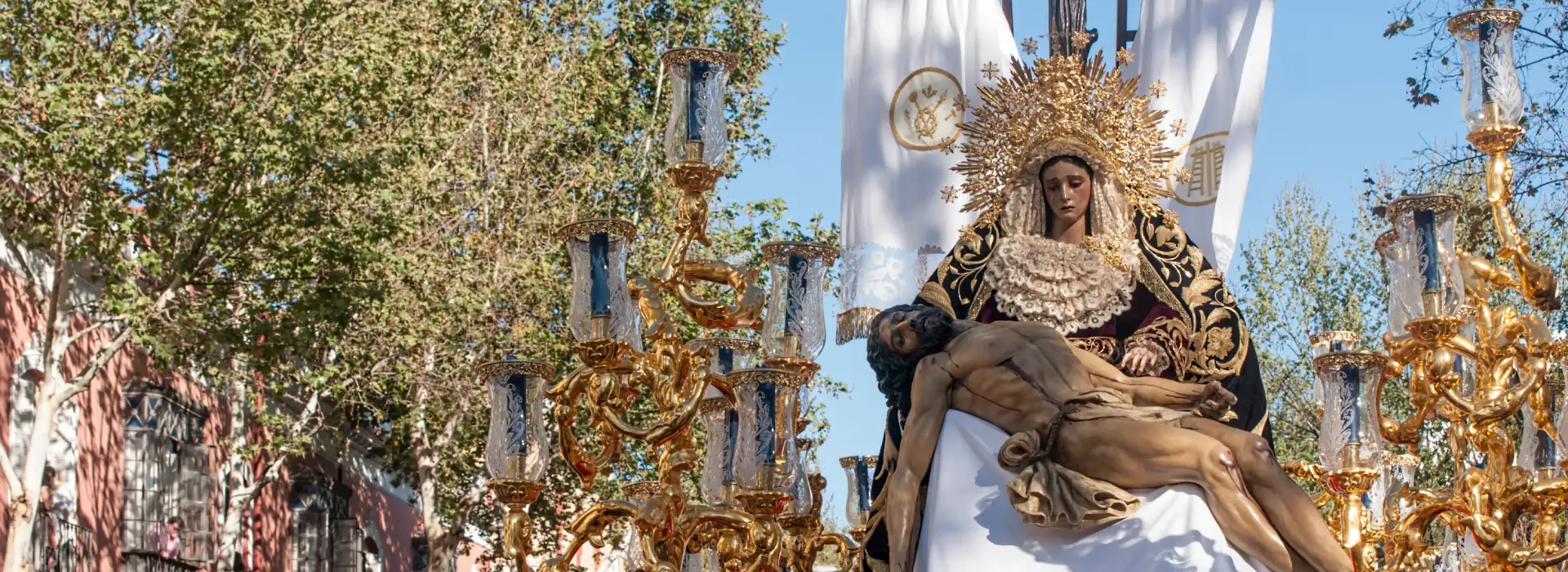 Procesi&oacute;n con imagen religiosa sobre un paso adornado con candelabros dorados.