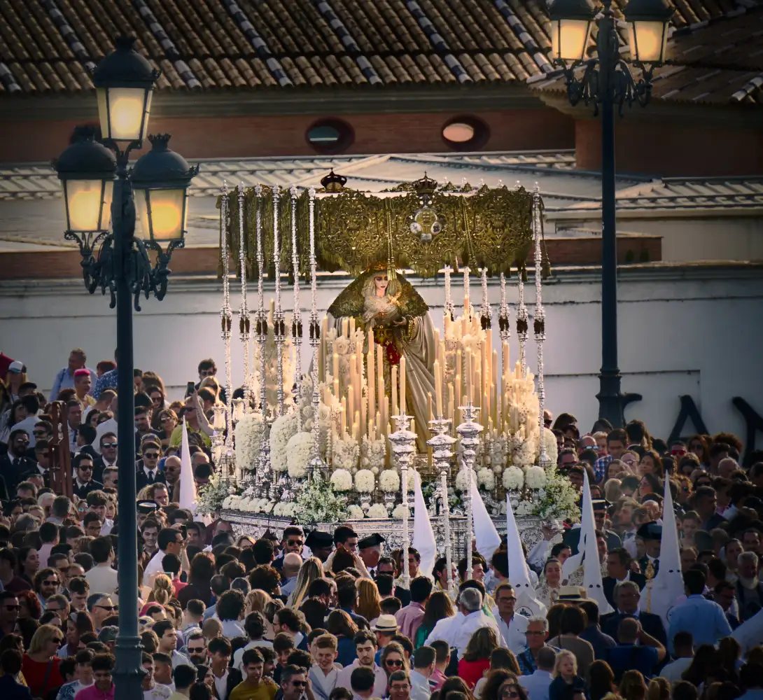 Procesi&oacute;n religiosa con un trono adornado con velas y flores blancas.