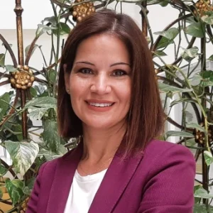 Mujer sonriendo frente a un fondo de plantas decorativas.