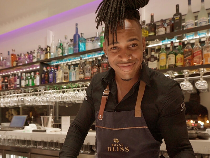 Bartender sonriente en un bar moderno con bebidas detr&aacute;s.