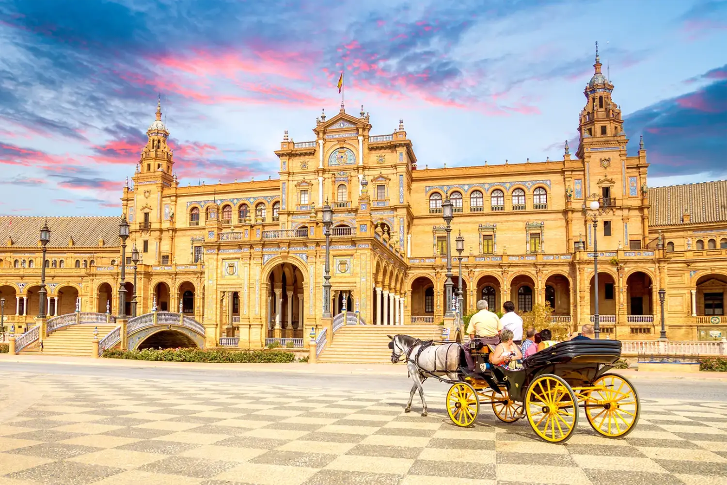 Plaza de Espa&ntilde;a en Sevilla, con cielo rosado y carruaje en primer plano.
