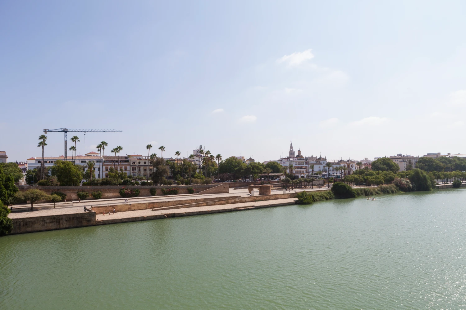 Vista de un r&iacute;o con edificios y una gr&uacute;a al fondo en un d&iacute;a soleado.