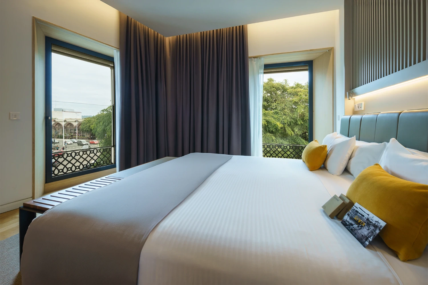 Habitaci&oacute;n moderna con cama doble, ventanas y cortinas oscuras.