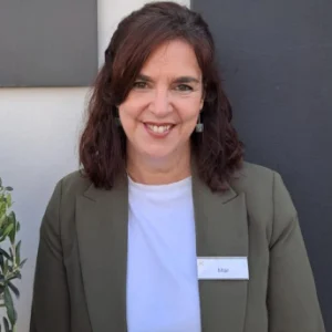 Mujer sonriendo con chaqueta verde y camiseta blanca.