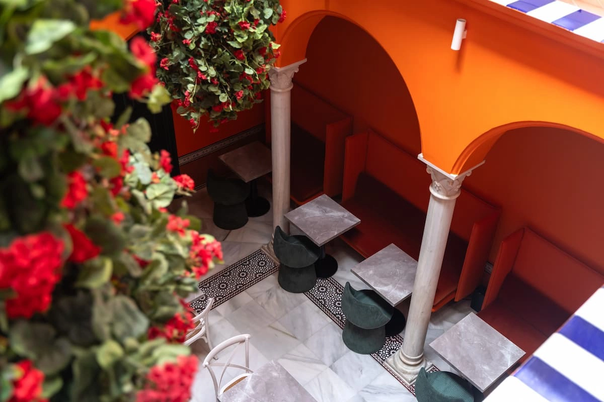 Patio interior colorido con mesas y sillas, rodeado de arcos y flores.