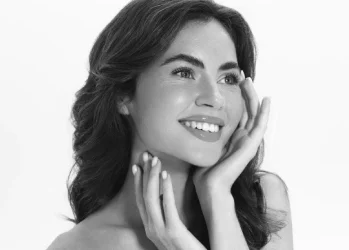 Mujer sonriente en retrato en blanco y negro, manos en el rostro.