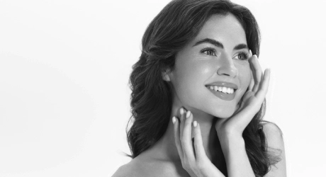 Mujer sonriente en retrato en blanco y negro, manos en el rostro.