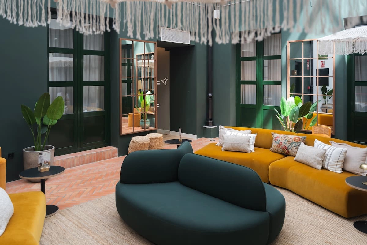 Sala moderna con sofás color verde y mostaza, decorada con plantas y cojines.