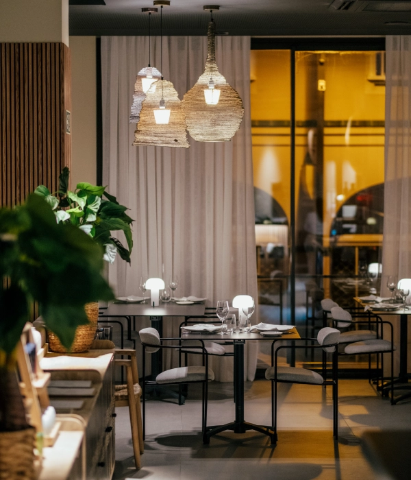 Comedor elegante con mesas, sillas y l&aacute;mparas colgantes en interior moderno.