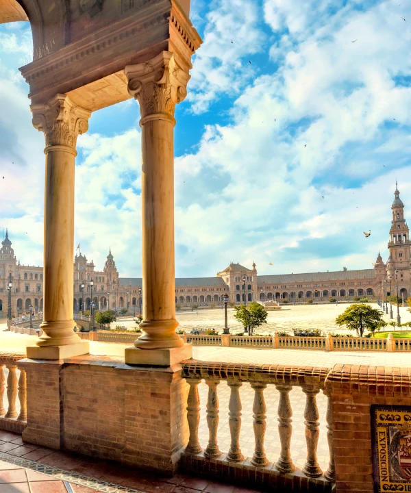Vista de la Plaza de Espa&ntilde;a en Sevilla con cielo azul y columnas en primer plano.