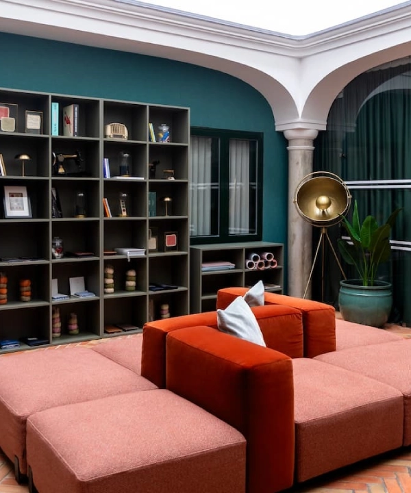 Sala moderna con sof&aacute; rojo, librero y l&aacute;mpara dorada.