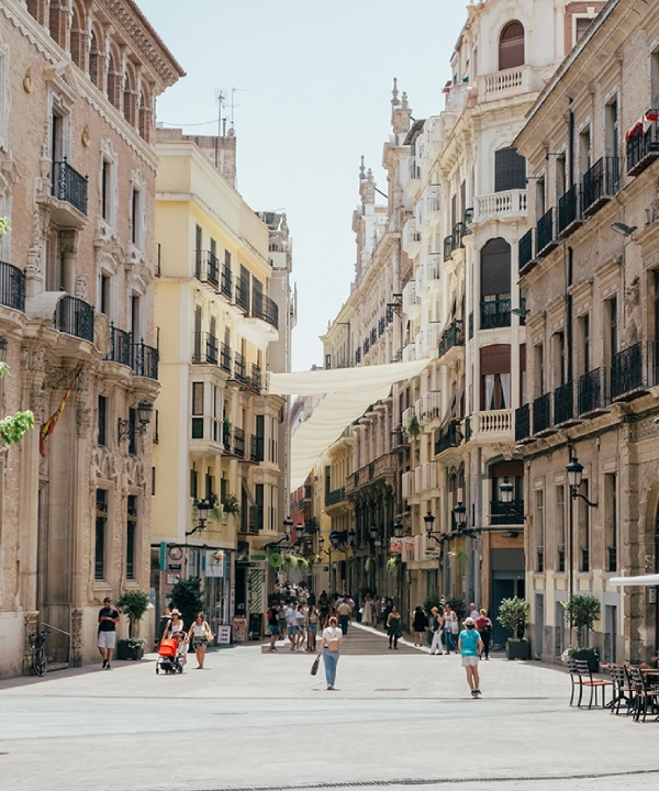 Calle con edificios antiguos y personas caminando bajo un toldo blanco.