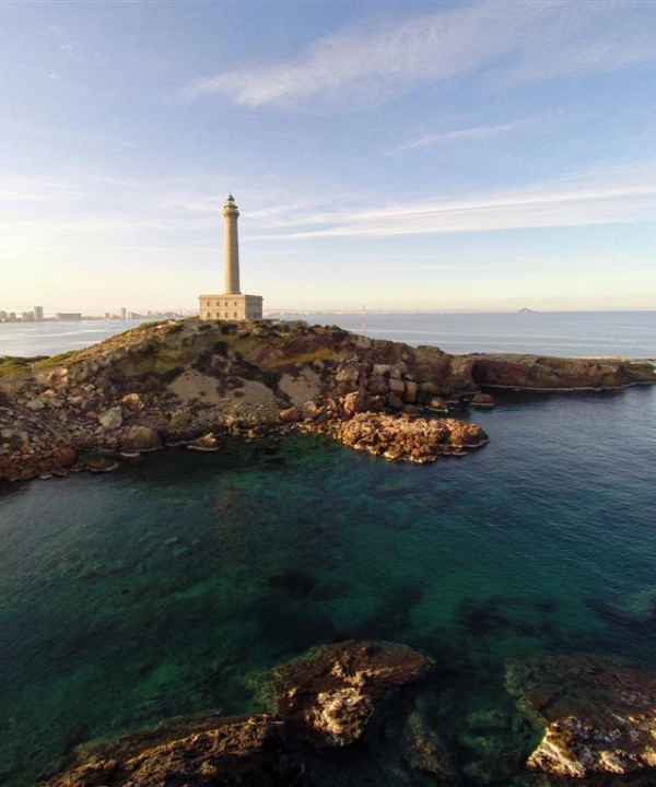 Faro en una colina rocosa junto al mar con cielo despejado.
