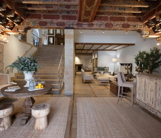 Sala r&uacute;stica con escaleras, mesa redonda y techos decorados con detalles.