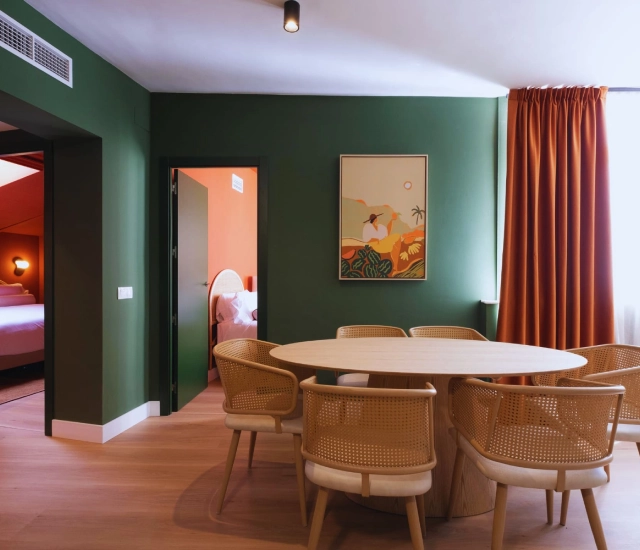 Sala con paredes verdes, mesa redonda, sillas de mimbre y cortinas naranjas.