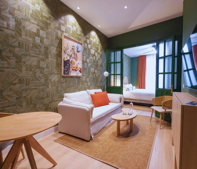Sala de estar acogedora con sof&aacute; blanco y acceso a dormitorio.