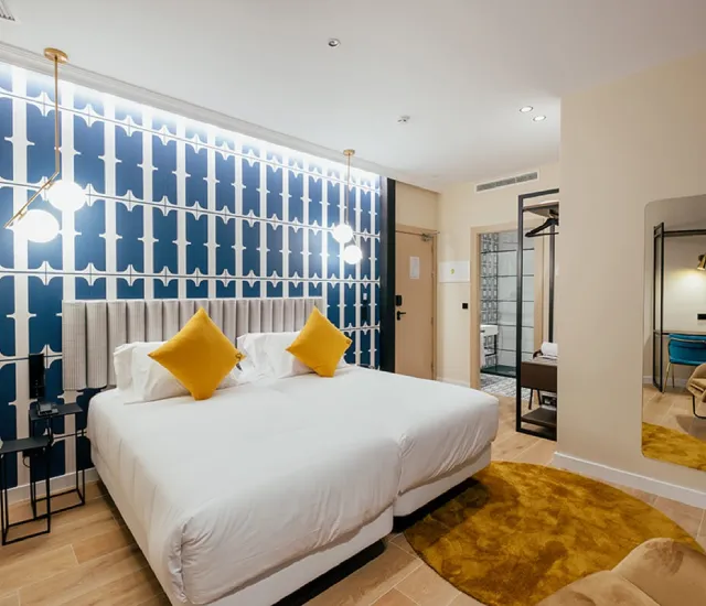 Habitaci&oacute;n moderna con cama doble, dos cojines amarillos y detalles en azul.