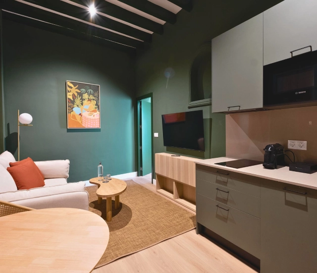 Sala moderna con paredes verdes y muebles de cocina, sof&aacute; y televisor.
