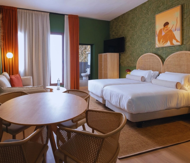 Habitaci&oacute;n de hotel moderna con camas, mesa y decoraci&oacute;n acogedora.