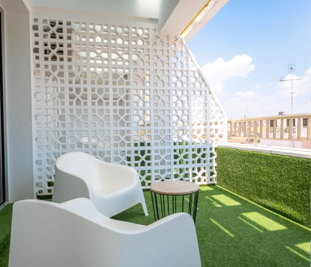 Terraza moderna con sillas blancas y mesa sobre c&eacute;sped artificial.