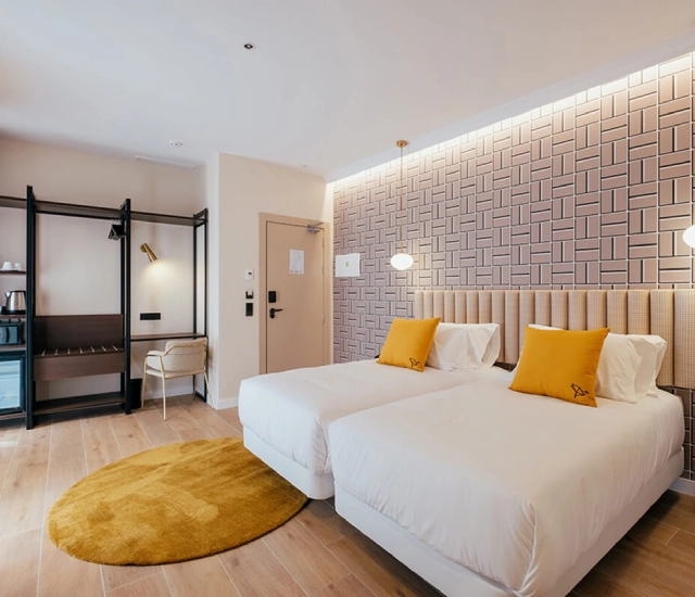 Habitaci&oacute;n moderna con dos camas, cojines amarillos y decoraci&oacute;n geom&eacute;trica.