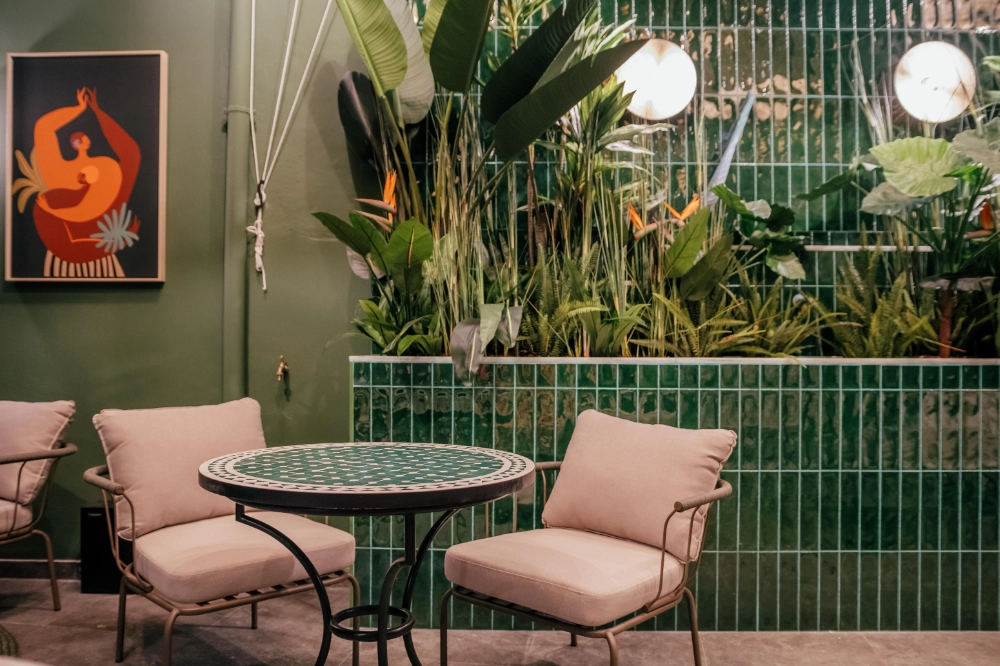 Sala con sillones, mesa redonda y pared verde con plantas decorativas.