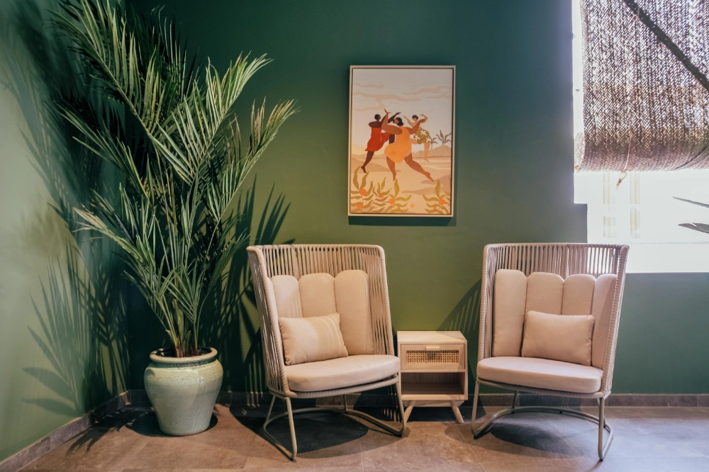 Dos sillones beige y una mesa auxiliar, con planta y cuadro en una sala.