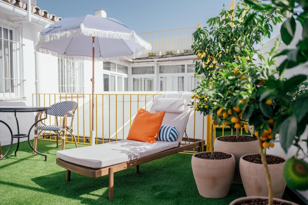 Terraza con tumbona, sombrilla y macetas junto a una planta verde.