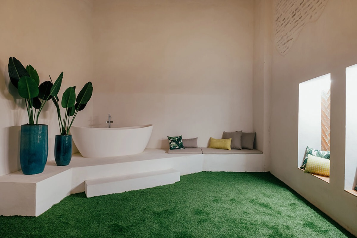 Baño moderno con bañera, plantas y suelos de césped artificial.