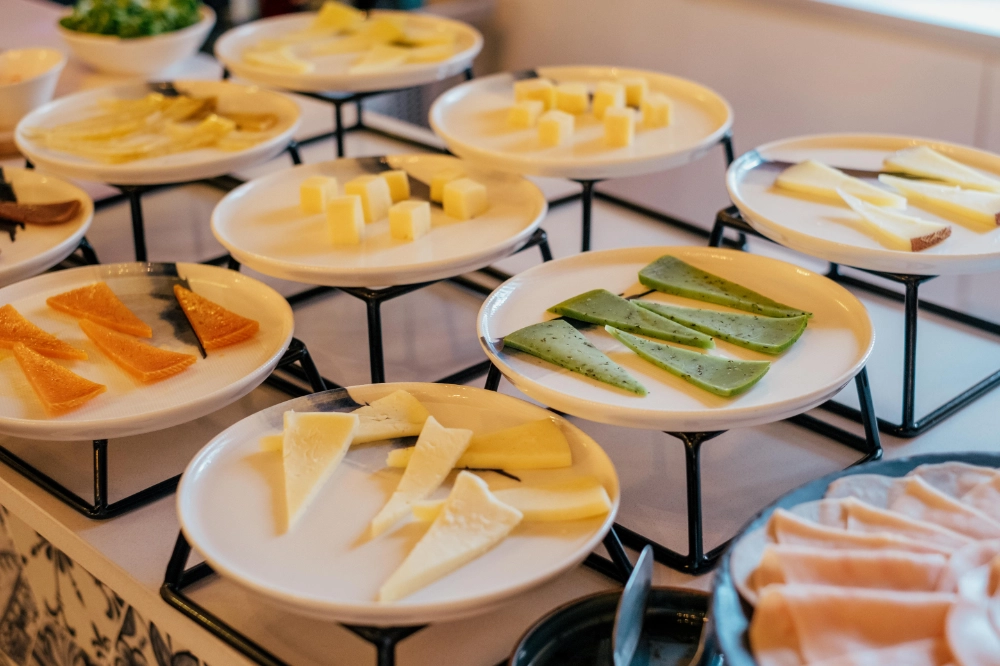 Variedad de quesos en platos blancos sobre un buffet.
