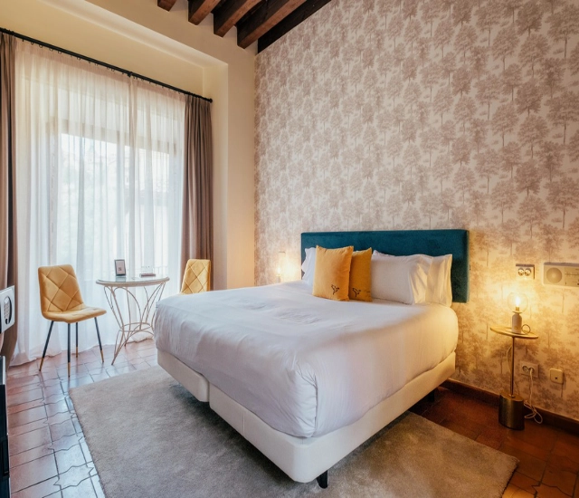 Dormitorio acogedor con cama grande, papel tapiz floral y luz c&aacute;lida.