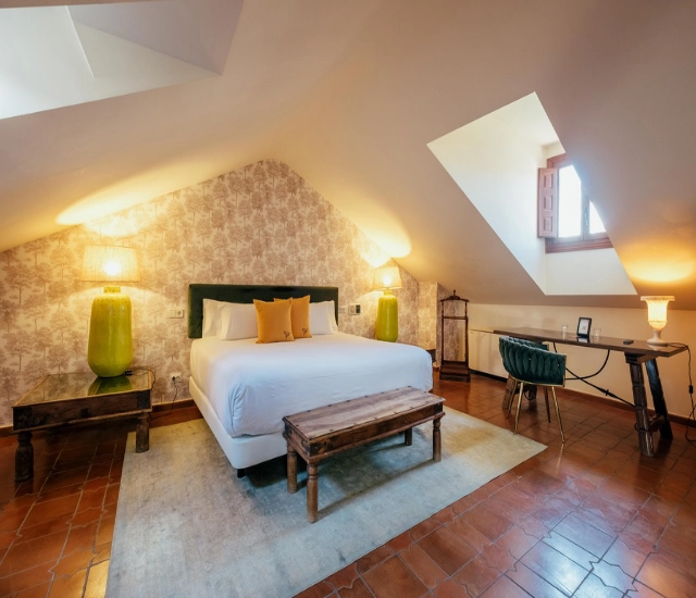 Habitaci&oacute;n abuhardillada con cama, escritorio y l&aacute;mparas decorativas.