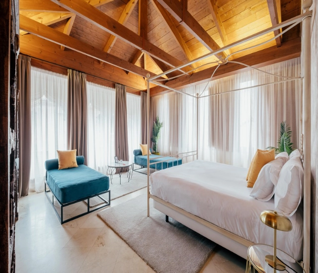 Habitaci&oacute;n con techo de madera, cama con dosel y sof&aacute; azul.