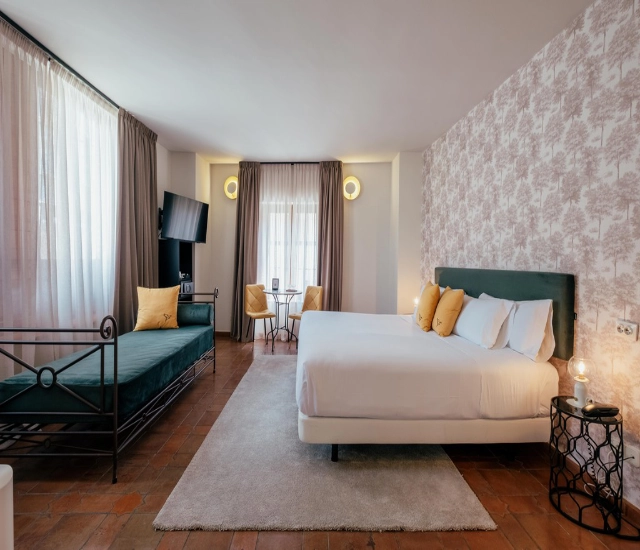 Habitaci&oacute;n moderna con cama matrimonial, sof&aacute;, televisor y luz natural.