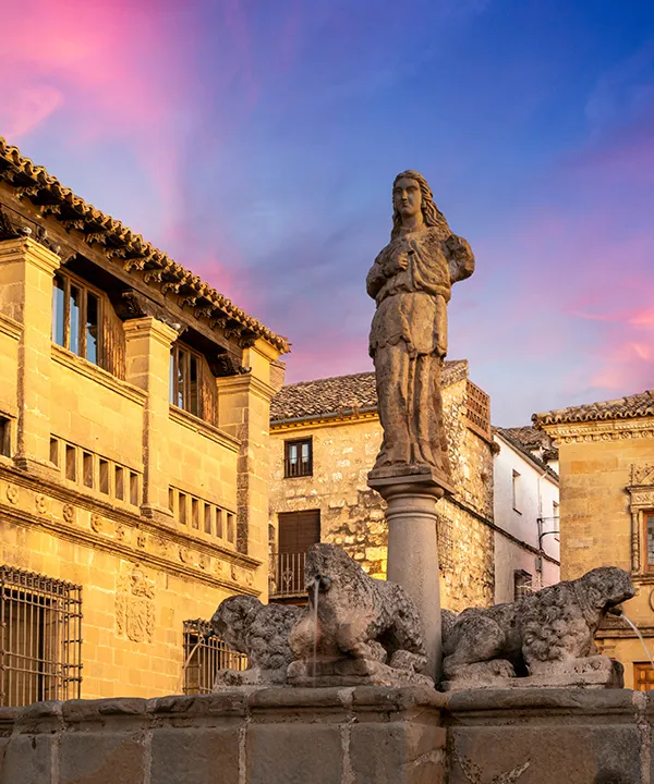 Estatua en fuente con edificios hist&oacute;ricos al atardecer.